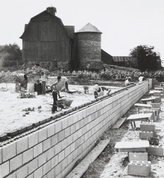 Building for a new “supermarket” food and household necessities store, under construction on the outskirts of the Milwaukee area. In the background is a barn and a silo.