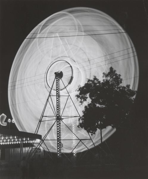 Illuminated wheel at night, probably at the Wisconsin State Fair, photographed by time exposure so that it appears as a whirl of light.