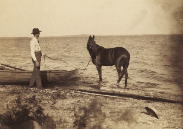 Charles M. Morris standing with his horse Penny at a lake shore at Morris Park.