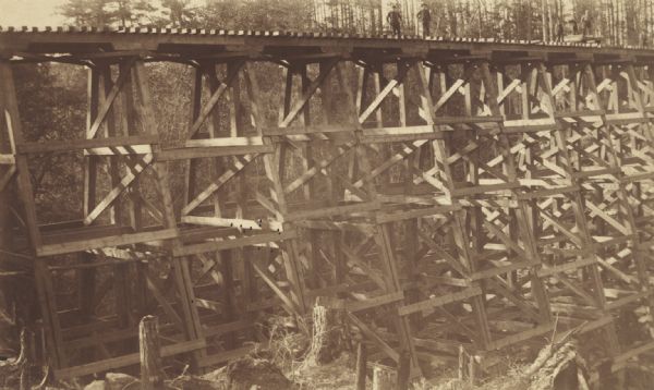 Timber railroad trestle over a wooded valley, apparently at the final stage of construction.