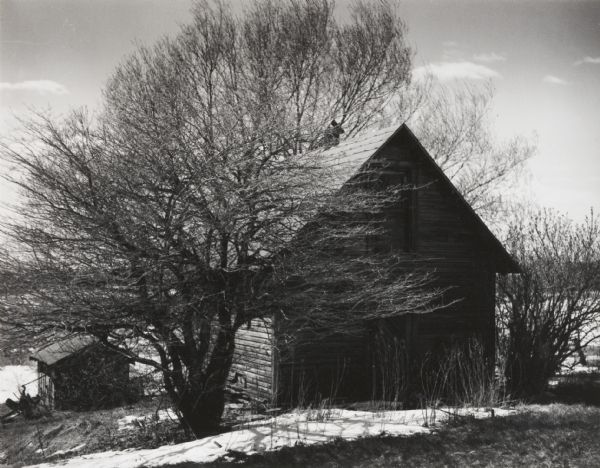 View of an abandoned farm and bare trees. Another small outbuilding is further down the hill on the left.

