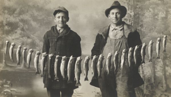 Man and boy with a string of fish posed in front of a painted backdrop.