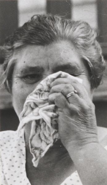 Close-up of a woman holding a handkerchief up to her face and weeping.