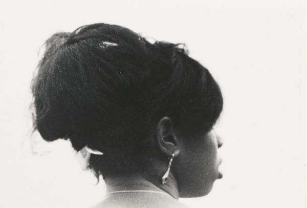 Informal portrait from a three-quarter back angle of a young African American woman showing the rather elaborately built-up hair style.
