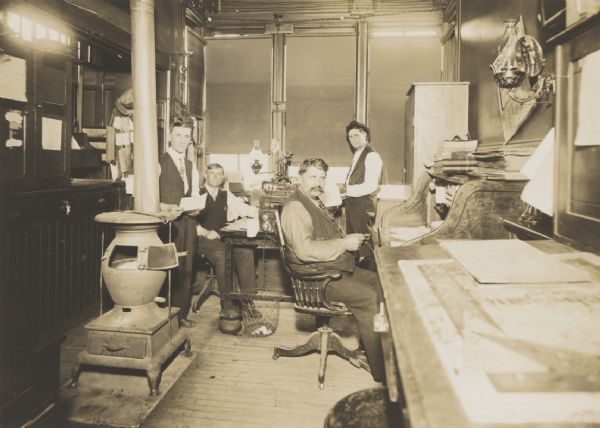 Interior, with four men, of a small office, very likely a railroad station office.