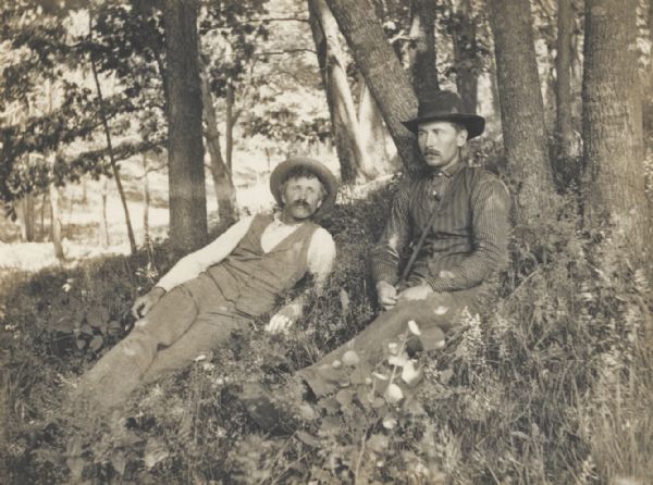 Two men reclining and resting in a wooded area “at Dorr Johnson's, Little Bear Valley,” Wis.