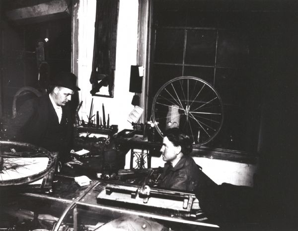 Two men in a repair shop, probably the repair shop of Leslie Werner. Leslie Werner is identified as the man wearing the hat on the left.