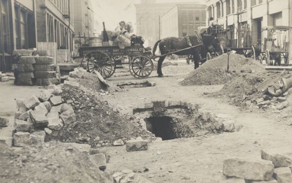 Street view showing horse-drawn wagons and excavations for underground utility (?) repairs.
