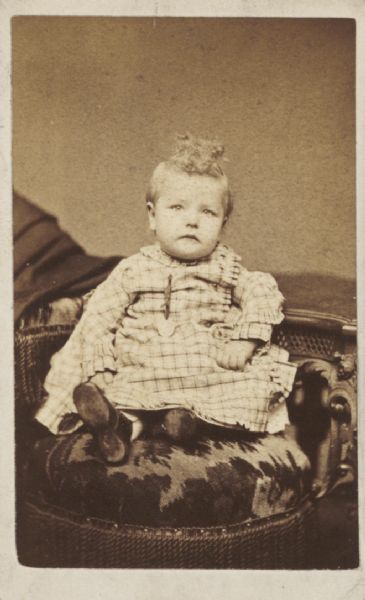 Carte-de-visite studio portrait of a small child sitting in a chair.

