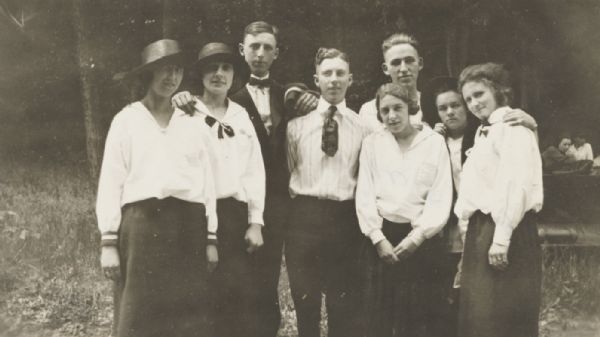 Posed group of eight young adults in an outdoor (woods or park?) setting.
