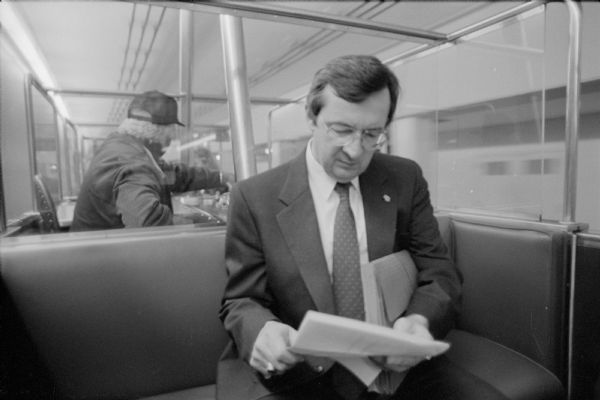Congressman David R. Obey of Wisconsin riding on the underground train that connects the Capitol with the legislative office buildings. A man in work clothes is seated behind him in a control booth.