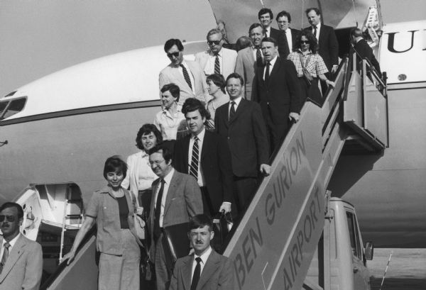 Members of a special House Appropriations Committee mission to the Middle East at the airport in Jerusalem. The committee was headed by Congressman David R. Obey of Wisconsin, chair of the Foreign Relations Subcommittee. Obey and his wife are on the first step of the stairs.  Also on the tour were Congressman Matthew McHugh, (directly behind Obey) and Congressman Thomas Petri of Wisconsin (behind McHugh). Above Petri, in the white jacket is Robert Kastenmeier, another Wisconsin congressman.