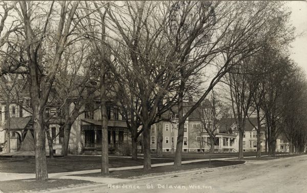 Angled view of the left side of a residential street lined with trees, probably taken in early spring. The home of A.H. Allyn is on the left. A covered fountain is in the Allyn yard. Caption reads: "Resident St. Delavan, Wis."