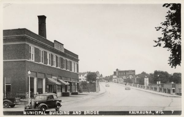 Municipal Building and Bridge View of the Municipal Building (City Hall), and a bridge lined with street lamps crossing the Fox River. Automobiles are driving along the street. Caption reads: "Municipal Building and Bridge, Kaukauna, Wis."