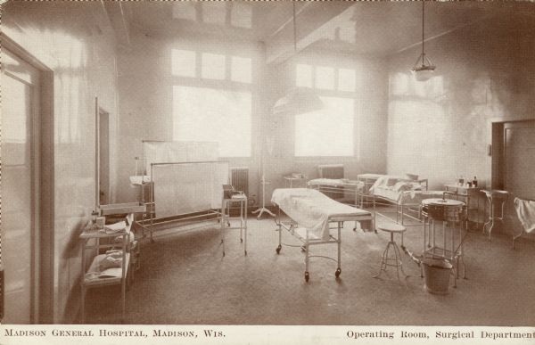 Interior view of a naturally lit operating room furnished with gurneys and tables for medical equipment. Caption reads: "Madison General Hospital, Madison, Wis. Operating Room, Surgical Department."