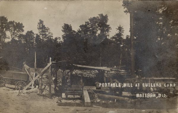 Portable Mill at Butler's Camp View of a portable mill, a wagon, and lumber in a forest clearing. Caption reads: "Portable Mill at Butler's Camp, Mattoon, Wis."