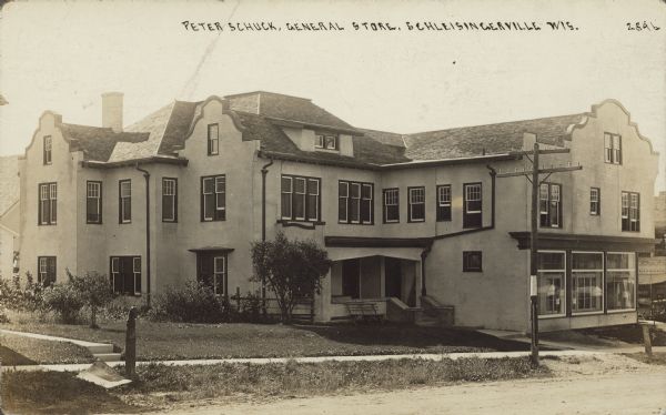 Peter Schuck General Store Text on front reads: "Peter Schuck General Store, Schleisingerville, Wis." Diagonal view of a general store with three large windows at the street. There are sidewalks along the unpaved street. The name of the town was changed to Slinger in 1921.