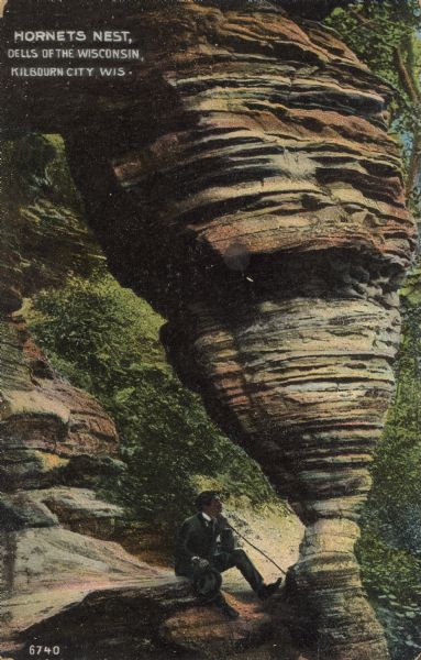 Hornet's Nest Text on front reads: "Hornet's Nest, Dells of the Wisconsin, Kilbourn City, Wis." The rock formation "Hornet's Nest" surrounded by trees and foliage with a man sitting at the base.<p>Kilbourn City was founded in 1857 by Byron Kilbourn, the name was changed in 1931 to Wisconsin Dells.</p>