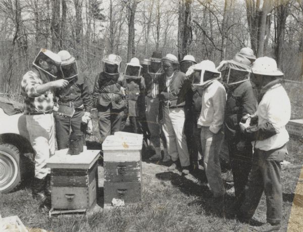 Beekeeping class in progress. All participants are wearing protective bee veils and hats, and some are wearing gloves. A crate or hive box in the background reads R.A. Lohry Appleton.