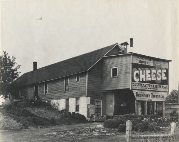 Exterior view of the Buckhorn Cheese Company plant. A sign painted on the exterior of the building reads: "Take One Home."