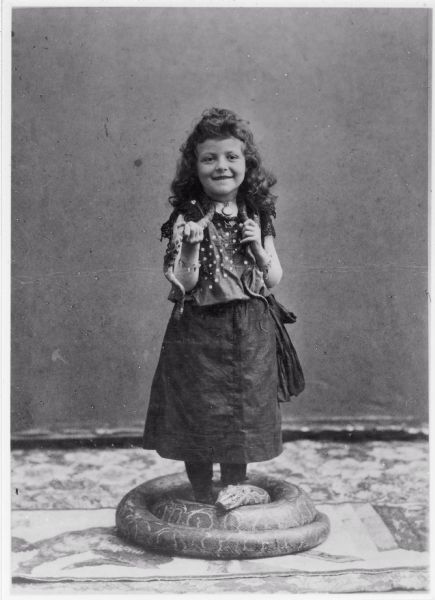 Grace May Hall, as a five-year-old circus child, with a large show python coiled at her feet and a smaller show snake around her neck.
