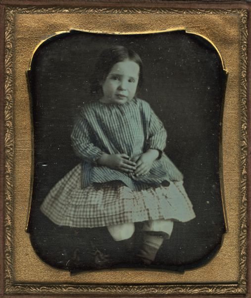 Sixth-plate daguerreotype of Ella or Irene Larkin as a child. Seated figure facing front with crossed ankles, wearing striped top and checked skirt. Hand-coloring on the cheeks and clothing. She was the daughter of Mr. and Mrs. B.F. Larkin. 
