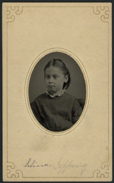 Selina Gopping Ferrotype/tintype of Selina Gopping as a young girl. Quarter-length portrait, seated, facing slightly left. She is wearing a dress or smock with plaid trim at neck and on sleeves, and white lace collar. Hand-coloring on cheeks and lips.