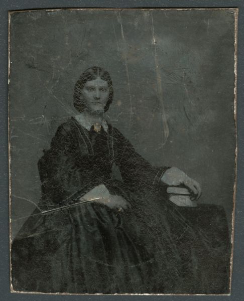 Harriet Hemans Brown Ninth plate ferrotype/tintype of Harriet Hemans Brown. Three-quarter length portrait, seated, facing forward, but torso turned to the right, with her hand on top of two books on a table. She is wearing a dark dress, white collar, and brooch at the neck. Hand-coloring on brooch and ring. Brown was a country school teacher from 1861-1865, at Ripon College in 1867, as well as a teacher in Fond du Lac, Wisconsin.