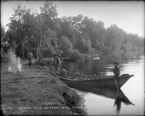 View along shoreline towards Indian log drivers, two in a bateau, and one man standing on the bank of the Chippewa River.