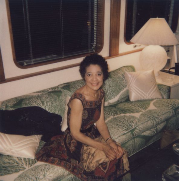Vel Phillips, wearing a patterned dress and sitting on a green and white tree-patterned couch.