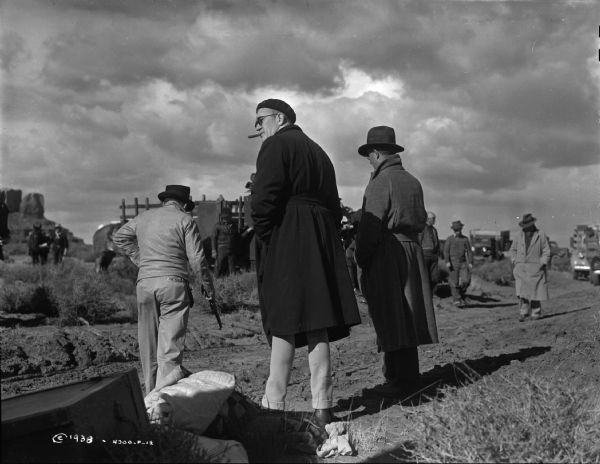 John Ford and crew on set Director John Ford is seen on the set of the 1939 film Stagecoach with many members of the film crew. Trucks can be seen in the distance and the sky is cloudy. Ford's back is to the camera but his head is turned to the side. He is smoking a cigar.