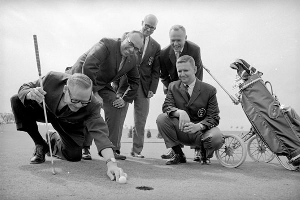 Madison Chamber of Commerce Sponsors Golf Outing Fran Conrad is shown with golf iron in hand as he measures a putt. He is general chairman of Tamisha, and is preparing for a golf and fun outing at the Lake Windsor Country Club. Other committeemen are watching. Left to right are: Gene Young, Millard Egre, James Langdon, and Jack Johnson.