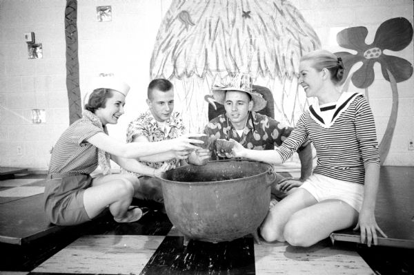 Sorority Party at the East Side Business Men's Association Clubhouse The traditional Alpha Chi Omega sorority South Sea islands party. Party attendees are (left to right): Donna Weber (Antigo); William T. Lorenz (Madison); Philip E. Pittz (Madison); and Nadine Ludwig (Medford). The wall behind them is painted with large flowers and a tropical thatch hut.