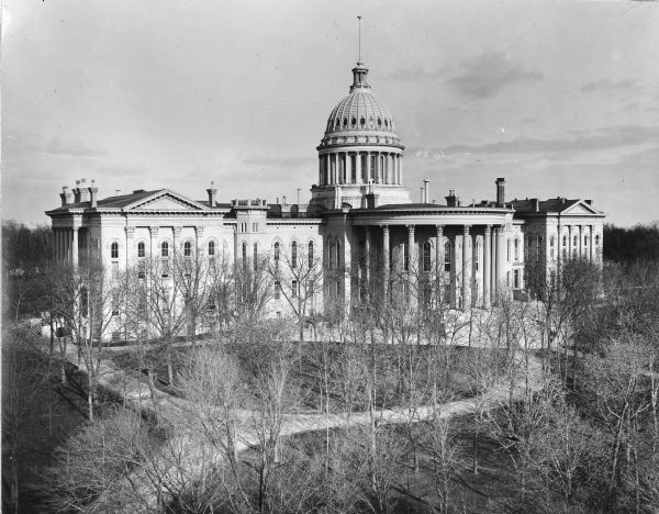 The expanded third Wisconsin State Capitol photographed at a time of the year when the trees in the park did not obstruct the view. As a result, the curvilinear walkways are also clearly visible. The Capitol Park was designed by noted landscape architect Horace W.S. Cleveland, but his design was only partially developed. This photograph is oriented with the North Wing addition at the left.