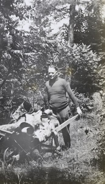 Man Pushing Wheelbarrow Filled with Birch Bark A man, wearing a turtleneck and pants, is pushing a wheelbarrow filled with birch bark on a grassy path under tall trees on the Island at Archibald Lake.