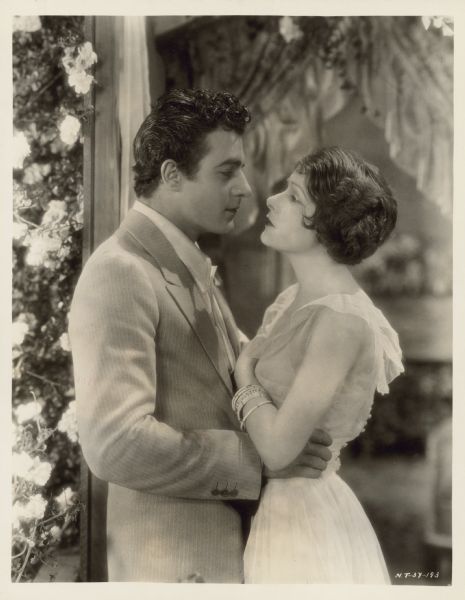 Norma Talmadge and Gilbert Roland in "Camille" Norma Talmadge and Gilbert Roland gaze into each other's eyes in a scene from the 1926 film "Camille".  He is dressed in a suit and she wears a light sleeveless dress.  The couple are outside and flowers are on the left.