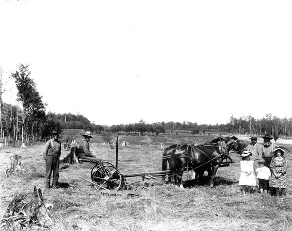 Four men and three children posing by a McCormick mower in a field.