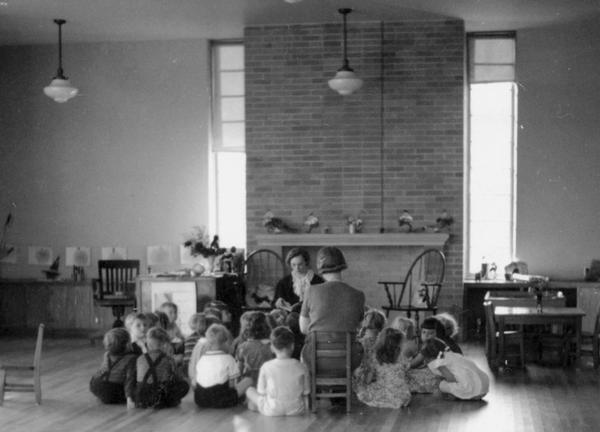 Students gathered closely around their teachers in the kindergarten room on the south end of the school. The open hearth, fireplace, high ceilings and windows all combined to create a positive learning atmosphere.