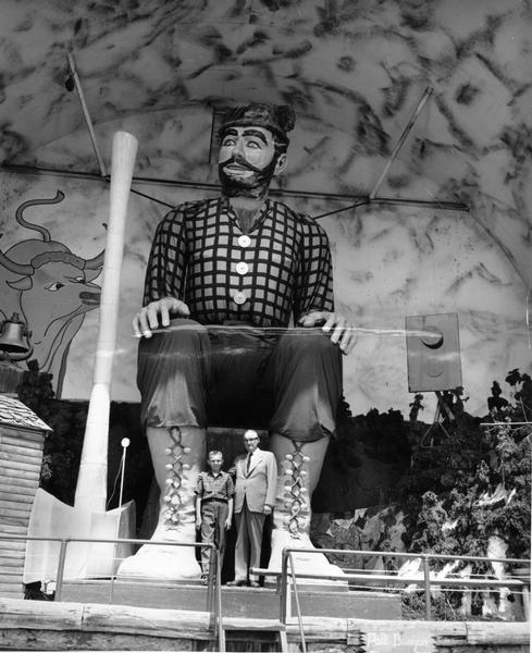 A man and boy pose in front of a giant Paul Bunyan statue.