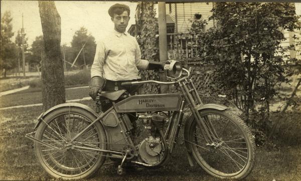 Dressed in his cycling outfit, Silas Wright Pifer poses next to his Harley-Davidson Motorcycle.