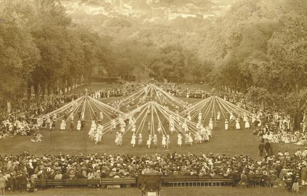 A view looking down on the Maypole Dance at the May Fete on Bascom Hill, showing dancers around four different Maypoles. In the foreground is the Lincoln Monument.
