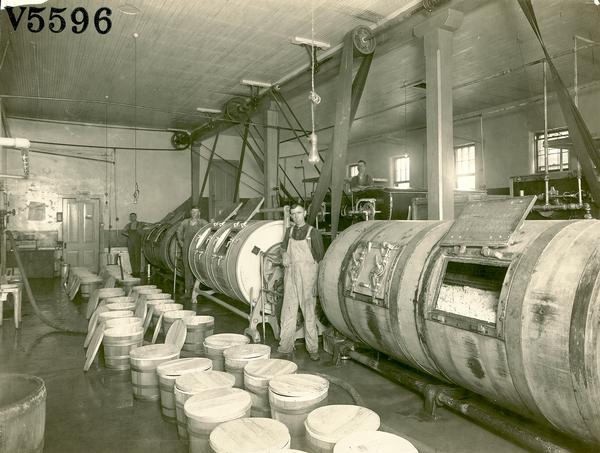 Two men pose at the Barron Coop Creamery next to the churns full of butter, which is ready to be packed into the small barrels nearby.