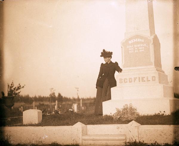 Cemetery monument of Charles Scofield. A woman dressed in black stands next to the monument.
