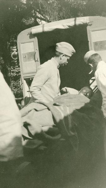 Medical personnel load a wounded Prussian into an ambulance. Captioned: "A wounded Prussian being loaded in my car for evacuation. He was shot just under his heart with an automatic, in a coup des mains (trench raid). Vaux Varennes.
