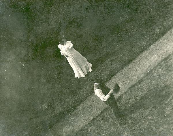 Overhead view of a man and woman on a pathway, she in white against a dark background, and he in shirt and vest.