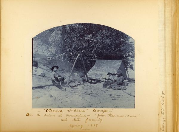 Beach fishing camp showing several people around a fire drying fish with a tent in the background.  Captioned: Ottawa Fishing Camp -- On the Island at Frankfort -- "John Wee-was-sum" and his family -- Spring 1889.  Cyanotype.