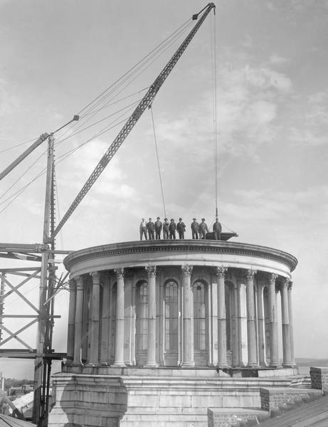 Workmen posing on the partially demolished dome of the third Wisconsin State Capitol, together with the hoist used for removing salvaged materials.  This demolition took place in preparation for the construction of the present Capitol.  The workmen were particularly careful with the destruction of the dome, as it was anticipated that it would be rebuilt on top of Bascom Hall.