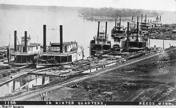 Elevated view of nine rafters wintering at Reed's Landing. At left is <i>Hiram</i> Price, with <i>L.W. Crane</i> beside her. Third is <i>Annie Girdon</i> with the <i>Union</i> behind her. Alongside the <i>Annie Girdon</i> is the <i>L.W. Barden</i>. Next to the <i>Union</i> is the <i>Clyde</i>, and next to it is a boat believed to be the <i>St. Croix</i>. At the extreme right is the <i>Silas Wright</i>, the only sternwheel rafter, all the rest are sidewheel rafters. Along the shoreline is a large raft of lumber.