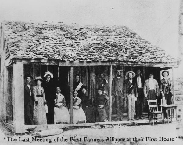 The first Farmers Alliance — also known as the Southern Alliance — is shown in front of the cabin in which their first formal meeting was held in 1877 in Pleasant Valley, Lampasas County, Texas. The cabin was uprooted and exhibited in the Chicago Exhibition of 1893. Later it was chopped up and pieces were passed out to the Populist partisans. Caption reads: "The Last Meeting of the First Farmers Alliance at their First House." Text in center below porch reads: "John Webber."