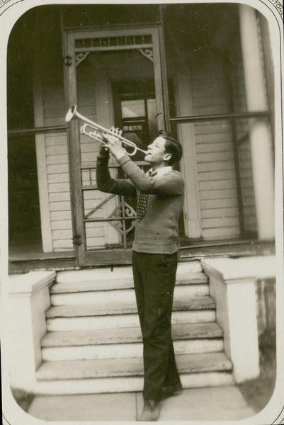 Gaylord Nelson during his high school years stands in front of a house playing the trumpet.